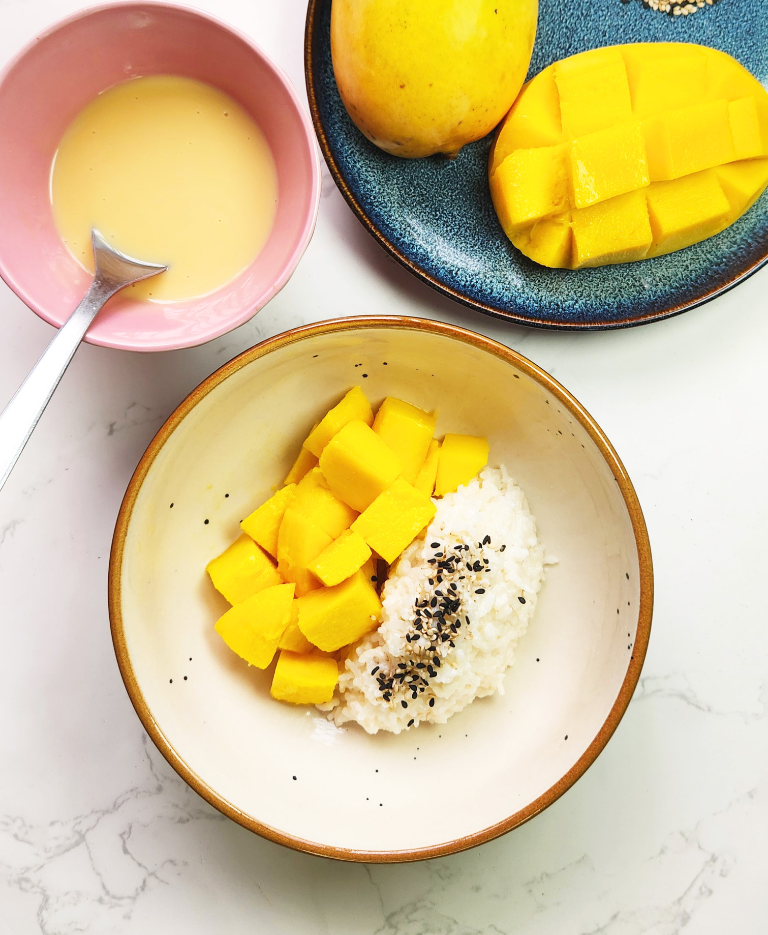 Thai mango sticky rice in a bowl with condensed milk sauce, mangoes, coconut sticky rice and sesame seeds