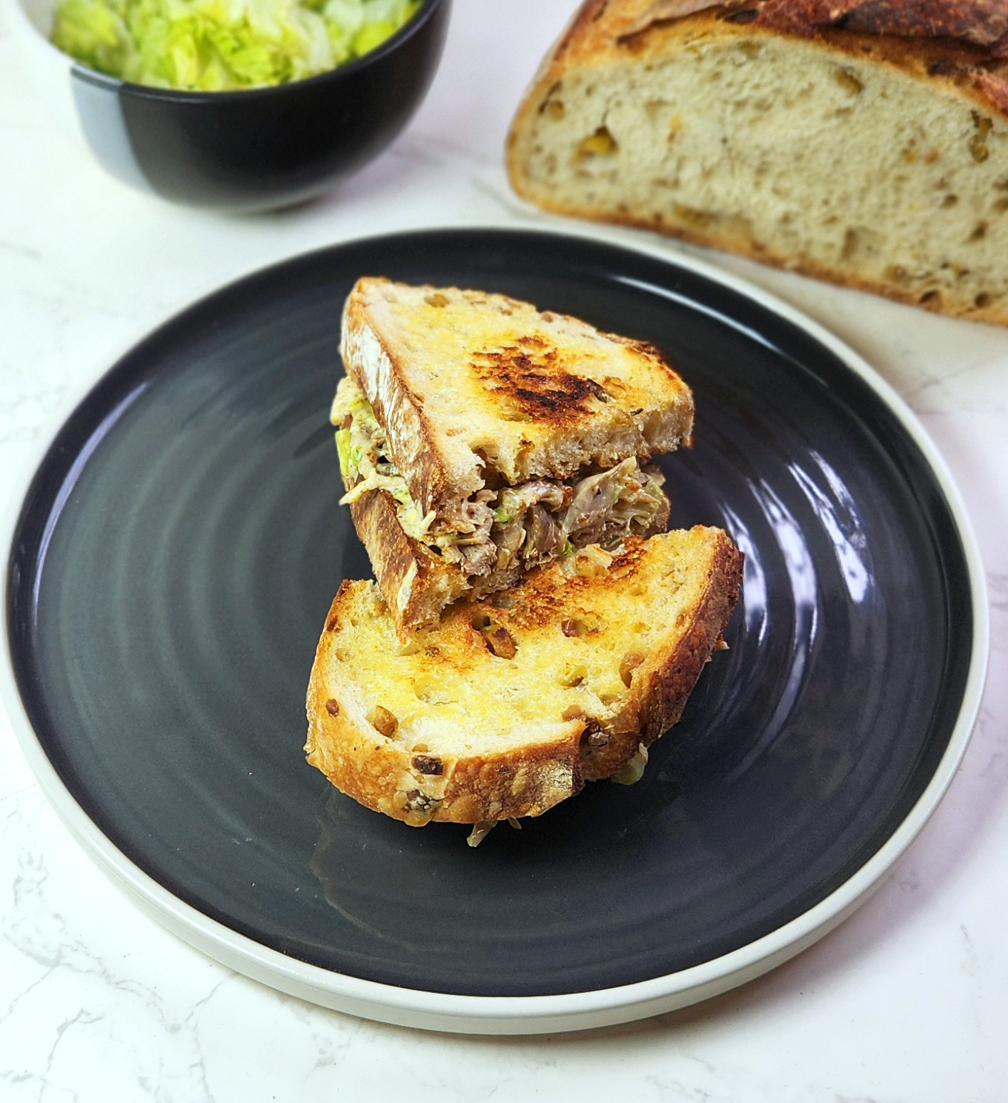 Chef's special Chicken Mayo Sandwich on a plate with sourdough loaf and lettuce in the background