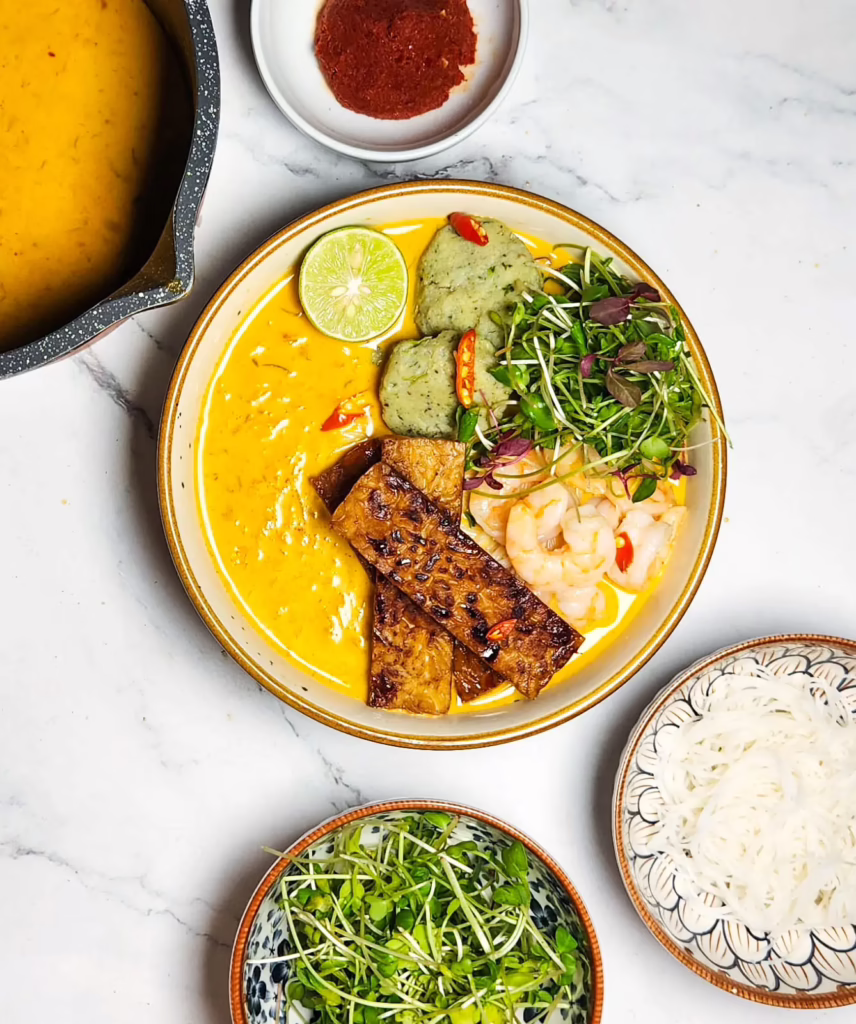 easy laksa recipe in a bowl with curry, tempeh, prawns, fish balls, bean sprouts and noodles