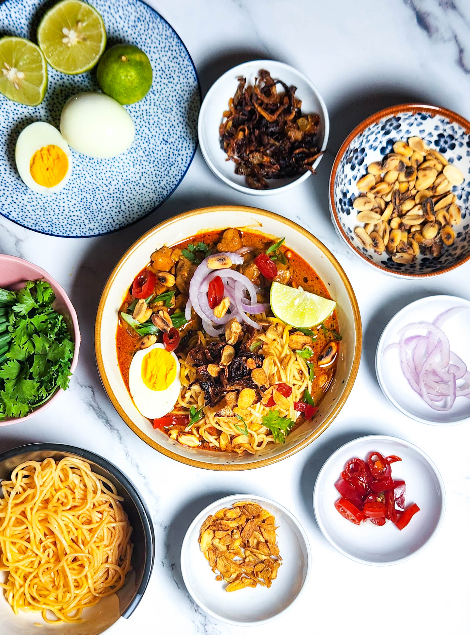 khow suey _ Burmese curry coconut noodle soup in a bowl with toppings lime, boiled eggs, onions, chillies, garlic